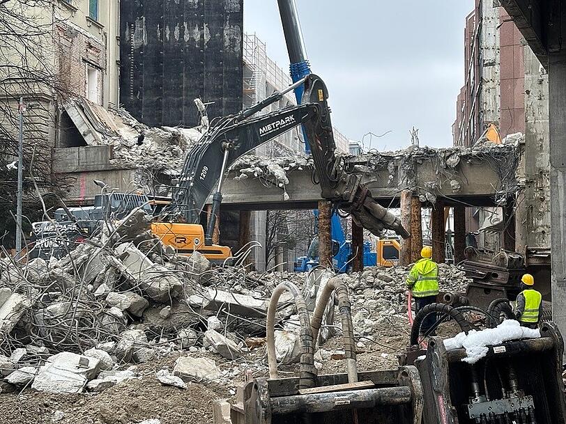 Ein Abbruchbagger bei der Arbeit. Die dunkle Plane links hinter ihm sch&uuml;tzt die denkmalgesch&uuml;tzten Nachbarh&auml;user.