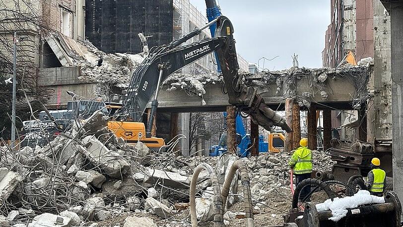 Ein Abbruchbagger bei der Arbeit. Die dunkle Plane links hinter ihm sch&uuml;tzt die denkmalgesch&uuml;tzten Nachbarh&auml;user.