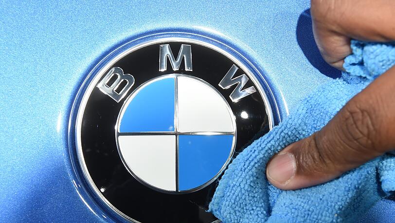 Ein Mitarbeiter einer Automesse poliert das Logo des Automobilherstellers BWM an einem Fahrzeug.
