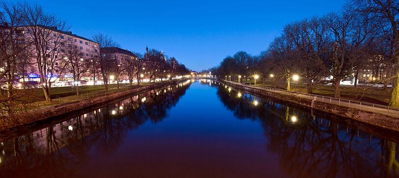 Idyllisches München: Der Abendhimmel und diverse Straßenlichter spiegeln sich auf der ruhigen Wasseroberfläche der Isar,