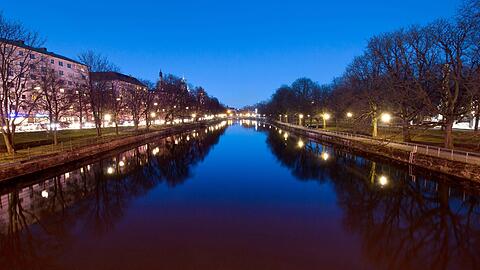 Idyllisches München: Der Abendhimmel und diverse Straßenlichter spiegeln sich auf der ruhigen Wasseroberfläche der Isar,