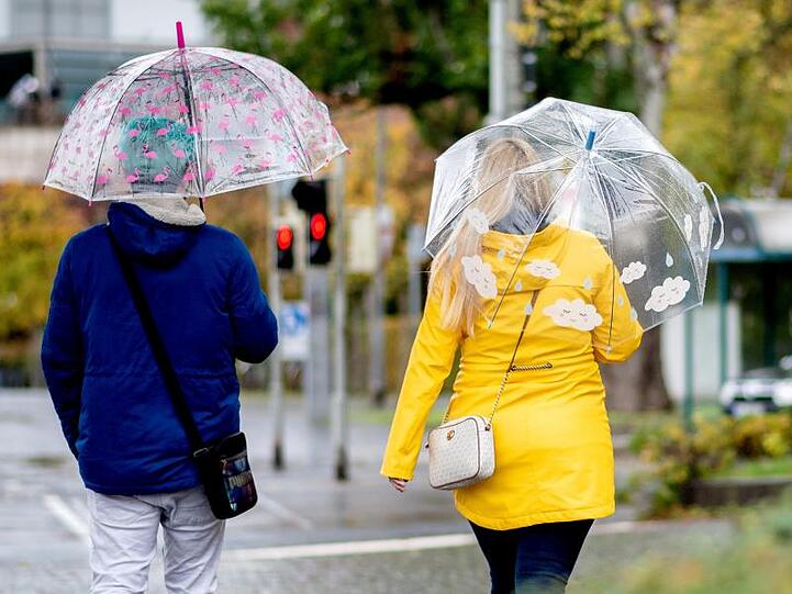 Zwei Passanten gehen mit Regenschirmen durch die Stadt. Foto: Hauke-Christian Dittrich/dpa/Archivbild