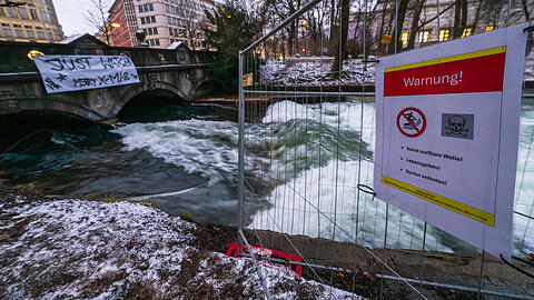 Ein Schild mit der Aufschrift "Warnung! - Keine surfbare Welle! - Lebensgefahr! - Surfen verboten!" ist an einem Zaun neben dem Eisbach und der provisorischen Eisbachwelle im Englischen Garten zu sehen. In den vergangenen zwei Monaten hatte sich die Welle nicht mehr aufgebaut. Seit dem ersten Weihnachtstag k&ouml;nnen Surfer wieder auf der stehenden Welle reiten.