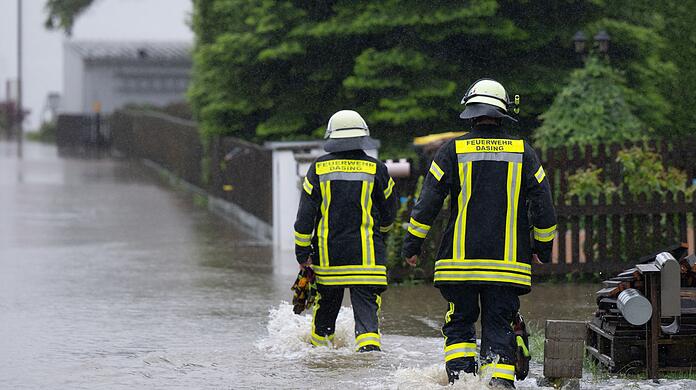 Feuerwehrleute gehen über eine überflutet Straße in Dasing.