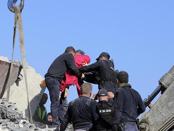 Rettungskräfte tragen die Leiche eines kleinen Mädchens in einer roten Decke aus einem zerstörten Gebäude.