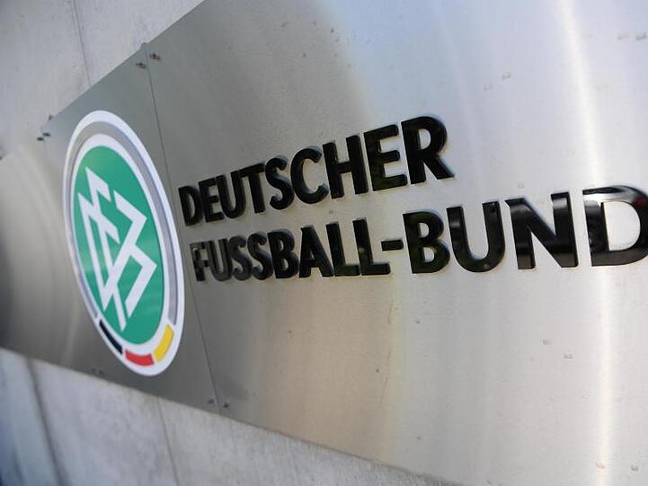 Logo und Schriftzug vor der Zentrale des Deutschen Fußball-Bundes (DFB) an einer Mauer. Foto: Arne Dedert/dpa/Archivbild