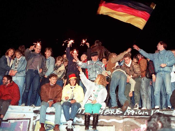 Mit Wunderkerzen in den Händen freuen sich die Menschen auf der Berliner Mauer über die Öffnung der deutsch-deutschen Grenze.