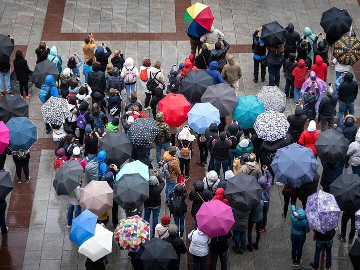 Touristen stehen bei Regen mit Schirmen auf dem Marienplatz. Foto: Sina Schuldt/Archiv