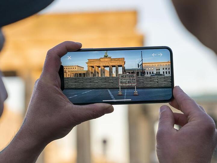 Apple-Chef Cook lässt sich am Brandenburger Tor von Entwickler Kolski das Projekt "MauAR" auf einem Handy erklären.