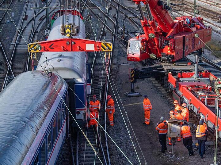 Gleisarbeiter arbeiten neben beschädigten Personenwaggons. Foto: Lino Mirgeler/dpa/Archivbild