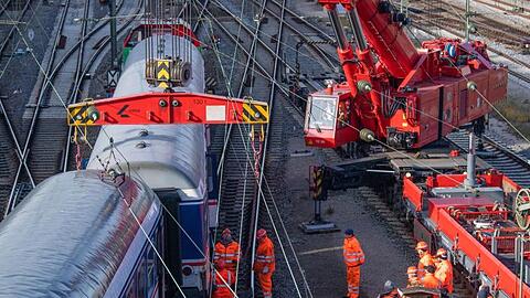 Gleisarbeiter arbeiten neben beschädigten Personenwaggons. Foto: Lino Mirgeler/dpa/Archivbild