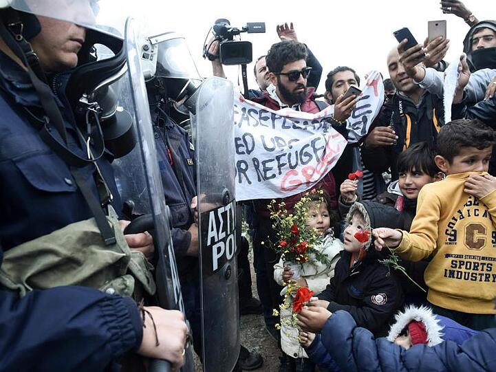 Kinder schenken Bereitschaftspolizisten nach den Zusammenstößen vor einem Flüchtlingslager im Dorf Diavata Blumen. Fotro: Giannis Papanikos/AP