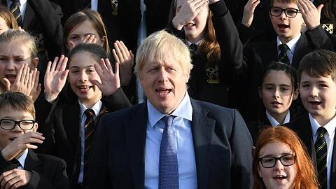 Großbritanniens Premierminister Boris Johnson (M) steht zwischen Schüler bei seinem Besuch eines Colleges.