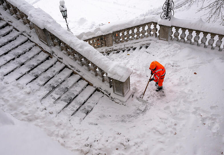 Mitarbeiter der Stadtreinigung schiebt am Friedensengel Schnee von der Freitreppe.