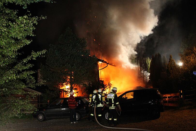 Im Hintergrund lodern die Flammen in dem Wohnhaus, vorne versuchen die Feuerwehrler, die Autos zu retten.