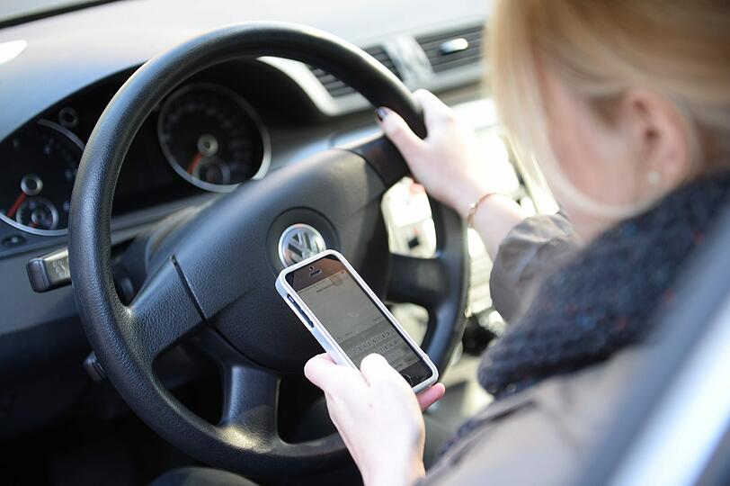 Auto am Steuer und liest Nachrichten auf ihrem Smartphone: Selfies und SMS am Steuer - Junge Erwachsene legen Handy nicht weg.