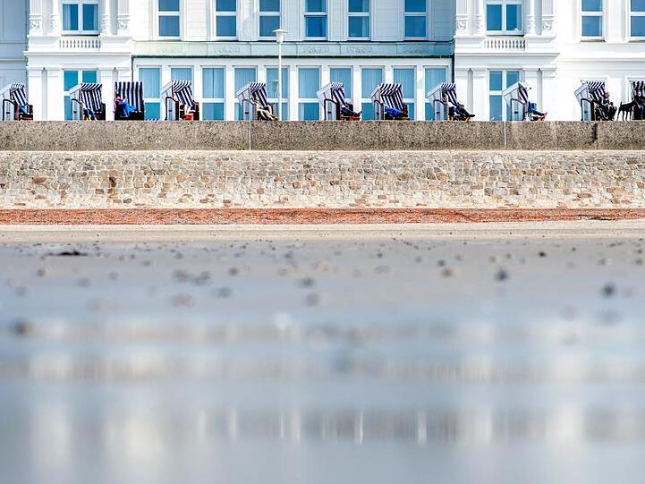 Touristen genießen die Sonne in Strandkörben auf der Strandpromenade am Weststrand auf Norderney.