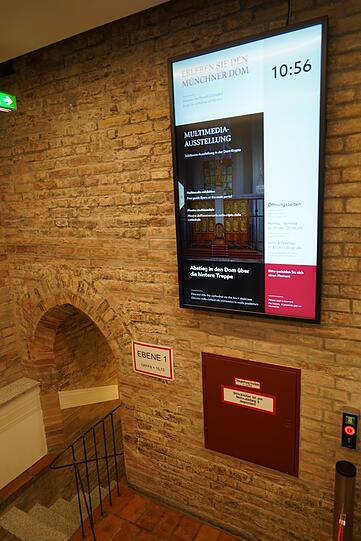 Warteraum vor dem Lift: gotische Ziegel und Info-Bildschirm.