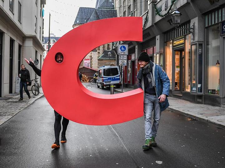 Ein Aktivist geht mit einem nachgebauten Buchstaben C aus dem Logo der CDU vor der Nikolaikirche in Leipzig über eine Straße.