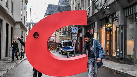 Ein Aktivist geht mit einem nachgebauten Buchstaben C aus dem Logo der CDU vor der Nikolaikirche in Leipzig über eine Straße.
