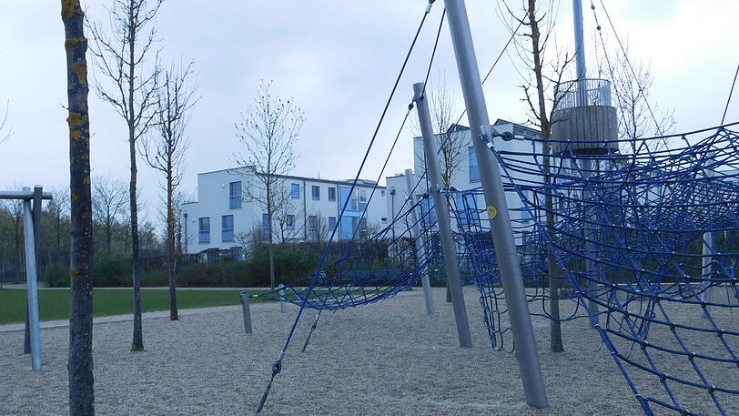 Vorne der Spielplatz, hinten Grünstreifen und Hecke.