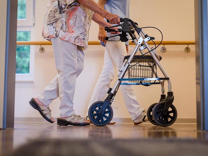 Eine Pflegekraft geht in einem Pflegeheim mit einer älteren Dame über einen Korridor. Foto: Christoph Schmidt/dpa/Symbolbild