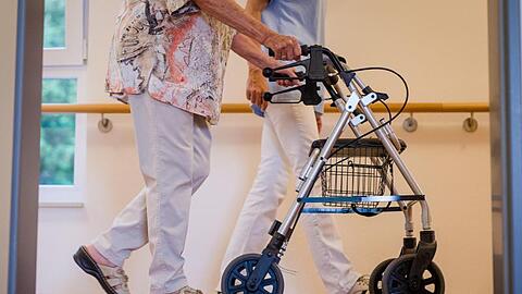 Eine Pflegekraft geht in einem Pflegeheim mit einer älteren Dame über einen Korridor. Foto: Christoph Schmidt/dpa/Symbolbild