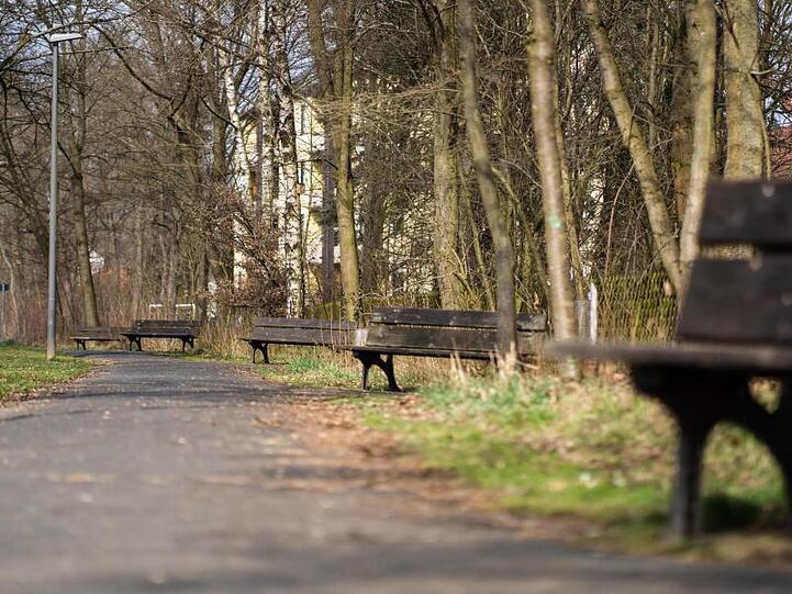 Die Sonne scheint auf leere Sitzbänke entlang eines Fußgängerweges. Foto: Nicolas Armer/dpa/Symbolbild