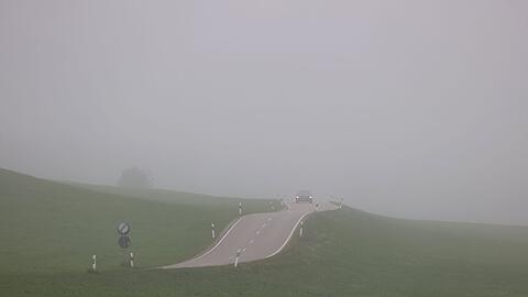 Ein Auto fährt durch die nebelverhangene Landschaft.