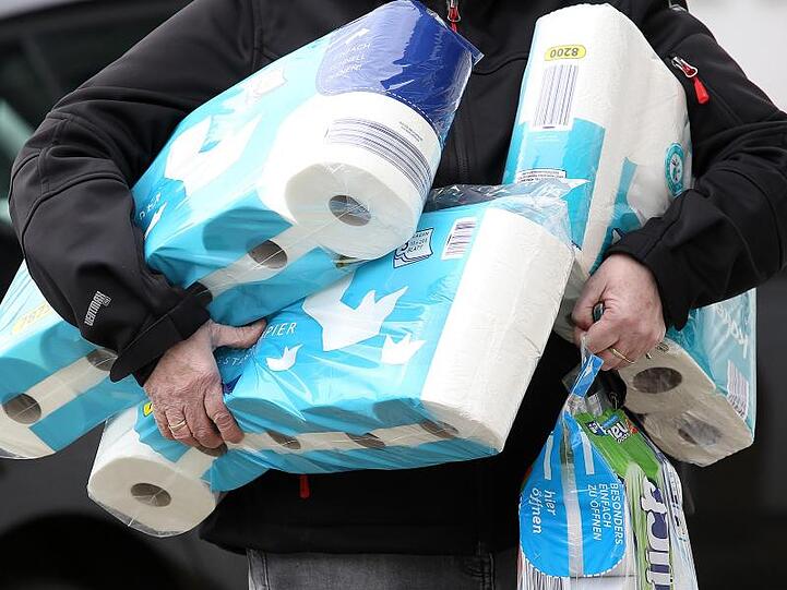 Ein Mann trägt Toilettenpapier und Küchenrollen aus einem Supermarkt.