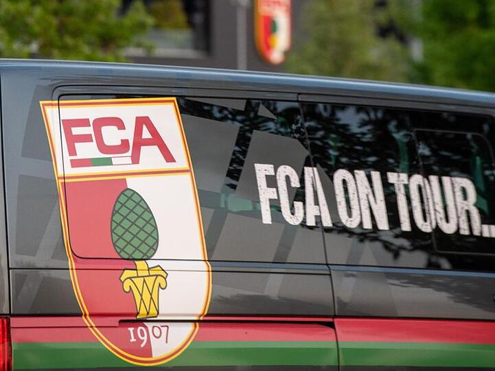 Auf einem Bus des FC Augsburgs, der vor der WWK-Arena steht, ist das Vereinslogo angebracht. Foto: Stefan Puchner/dpa