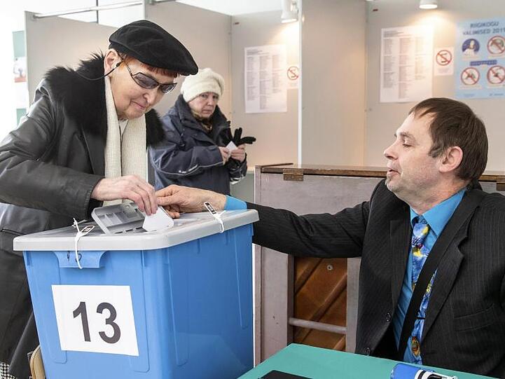 Ein Mitarbeiter der Wahlkommission hilft in einem Wahllokal in Tallinn einer Frau bei der Stimmabgabe.