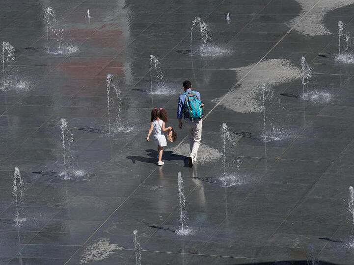 Vater und Tochter holen sich eine Abkühlung an Wasserfontänen.