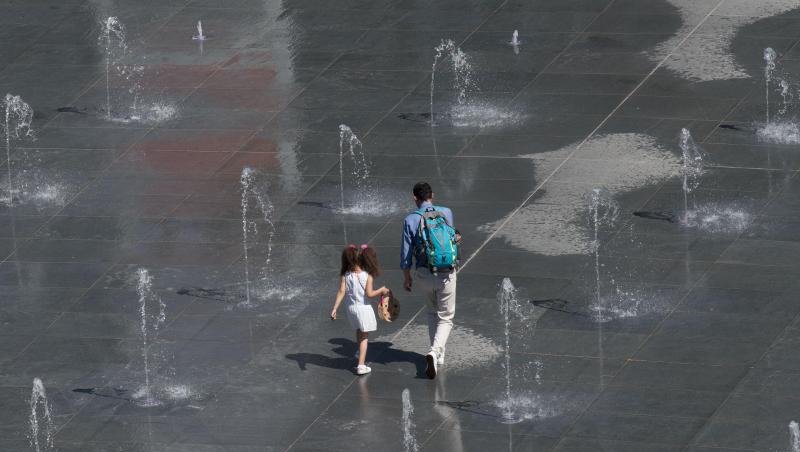 Vater und Tochter holen sich eine Abkühlung an Wasserfontänen. Vater und Tochter holen sich eine Abkühlung an Wasserfontänen.