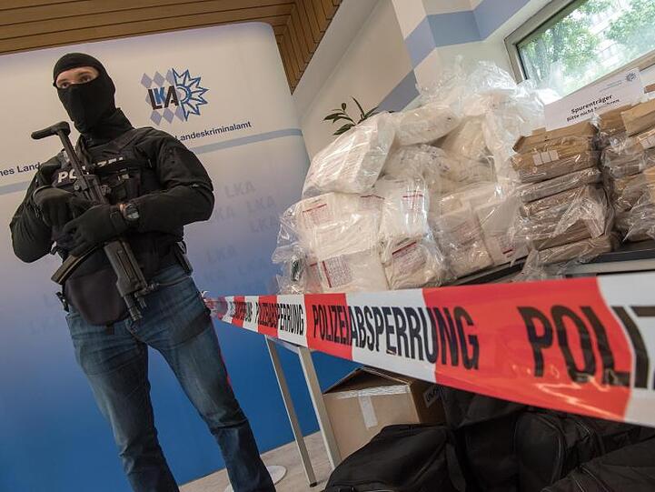 Ein schwer bewaffneter und vermummter Polizist bewacht während einer Pressekonferenz im bayerischen Landeskriminalamt etwa 640 Kilo Kokain, Waffen und Bargeld.