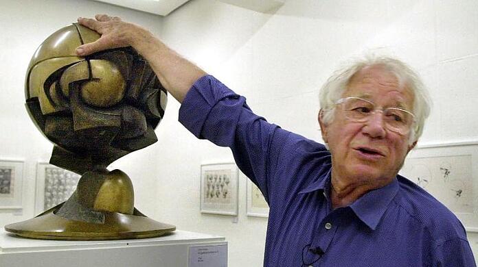 Der Bildhauer Fritz Koenig (1924-2017) legt seine Hand auf das Modell seiner Skulptur "The Sphere".