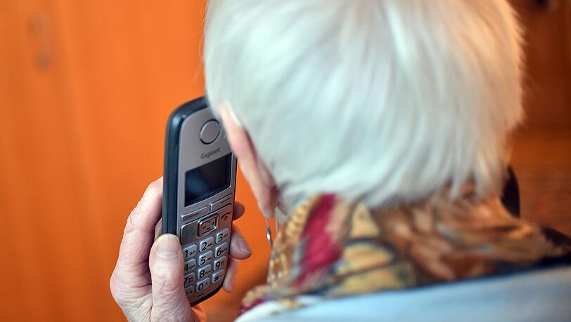 Eine Seniorin hält einen Telefonhörer an ihr Ohr.