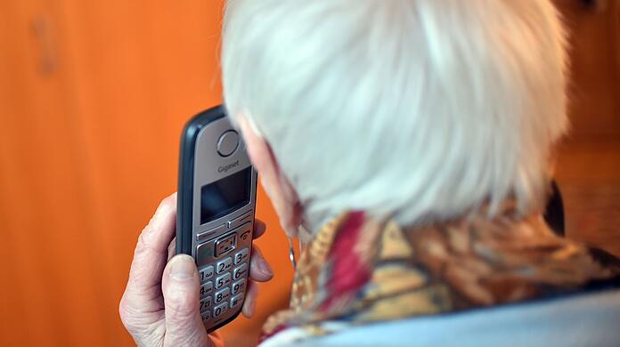 Eine Seniorin hält einen Telefonhörer an ihr Ohr.