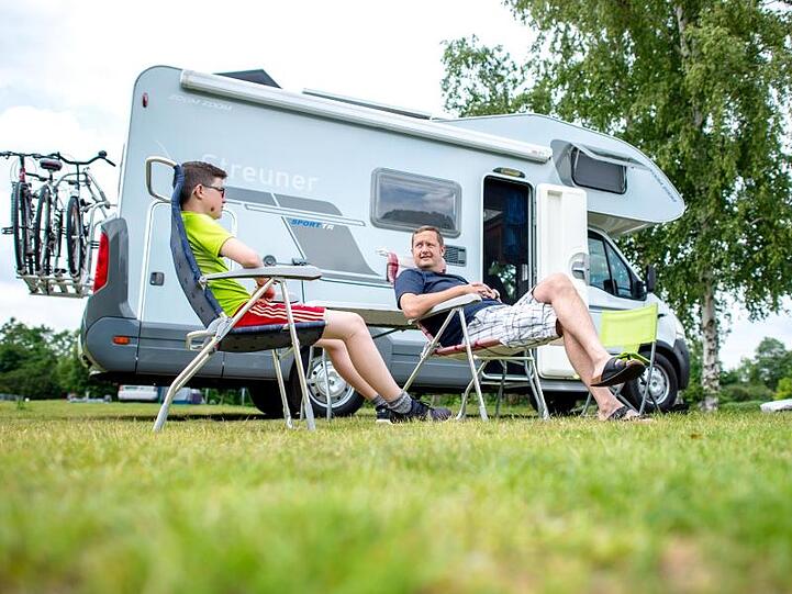Urlauber aus Bayern sitzen auf einem Campingplatz vor ihrem Wohnmobil. Foto: Hauke-Christian Dittrich/dpa/Archivbild