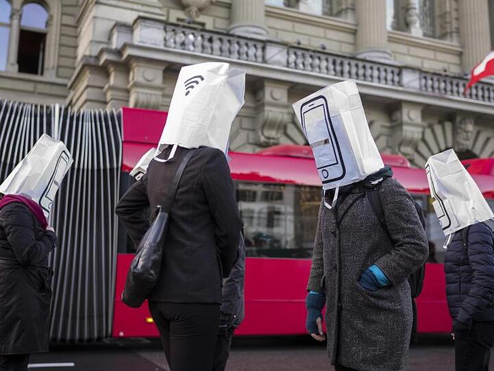 Aktivisten mit Papiertüten auf dem Kopf, auf denen Mobiltelefone abgebildet sind, warnen während der Nationalratssitzung vor dem Ausbau des Mobilfunknetzes auf den 5G Standard.