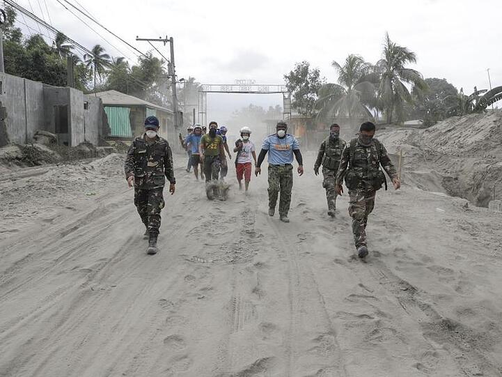Philippinische Polizisten und Soldaten laufen auf einer mit Vulkanasche bedeckten Straße.