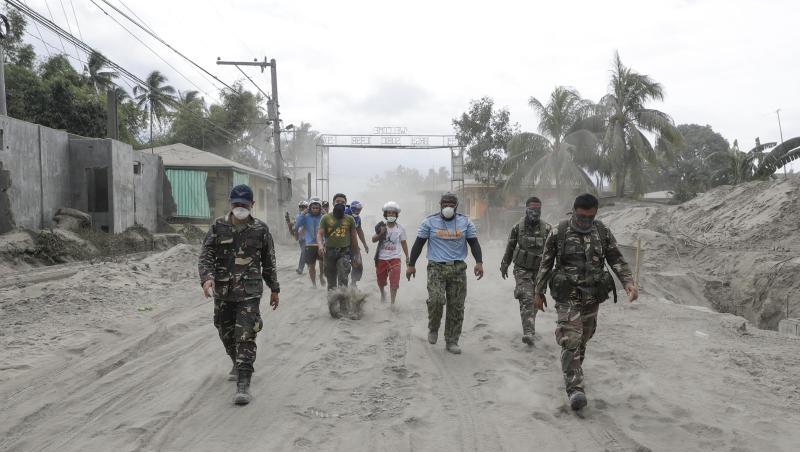 Philippinische Polizisten und Soldaten laufen auf einer mit Vulkanasche bedeckten Straße. Philippinische Polizisten und Soldaten laufen auf einer mit Vulkanasche bedeckten Straße.