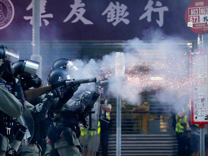 Polizisten mit Gasmasken schießen Tränengas auf Demonstranten.
