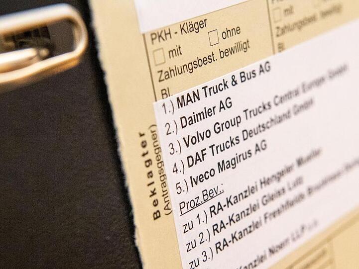 Akten mit den Namen der beklagten Firmen und ihrer Anwälte stehen vor Beginn des Prozesses im Gerichtssaal. Foto: Lino Mirgeler/dpa/Archivbild
