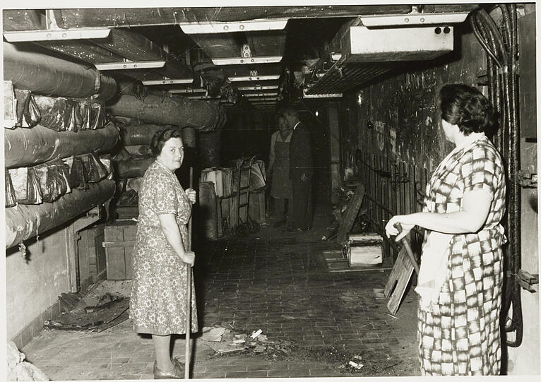 1961: Zwei Damen in Kittelschürze trocknen im Heizungskeller des ehemaligen Führerbaus durch Löschwasser beschädigte Akten aus dem Staatsarchiv.