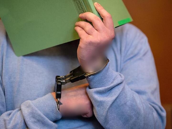 Der Angeklagte sitzt mit einem Aktendeckel vor dem Gesicht auf der Anklagebank im Gerichtssaal. Foto: Swen Pförtner