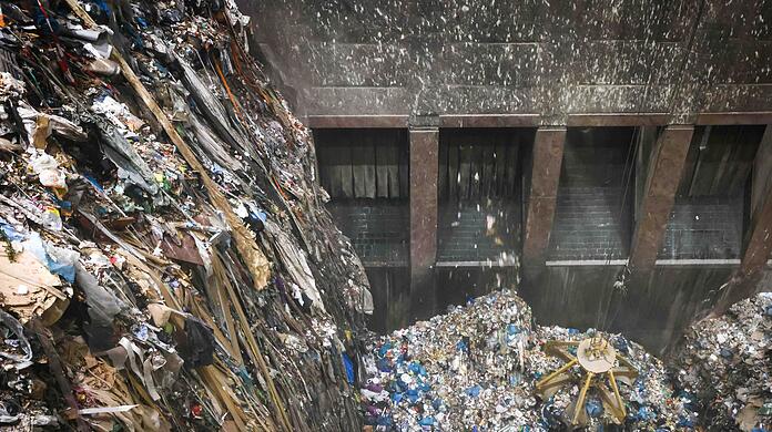 Mit einem großen Greifer sortiert und lockert ein Kran den angelieferten Abfall im Müllbunker einer Müllverwertungsanlage.