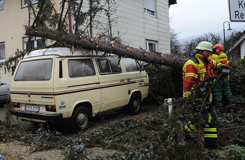 Feuerwehrmänner entfernen am Donnerstag (05.01.2012) in Kirchzarten (Landkreis Breisgau Hochschwarzwald) einen Baum, der auf einem Fahrzeug liegt. Sturm "Andrea" sorgt im Schwarzwald für umgestürzte Bäume.