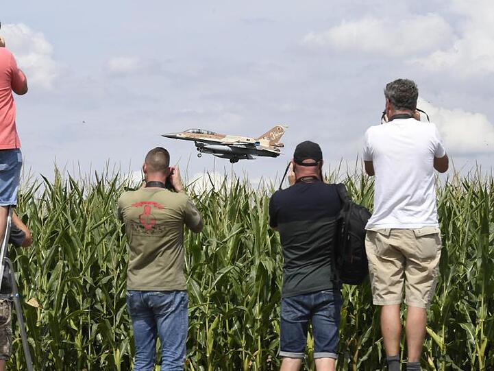 Ein israelischer F-16 Bomber landet auf dem Fliegerhorst Nörvenich im Kreis Düren, beobachtet von mehreren Männern mit Kameras, die an einem Maisfeld stehen.