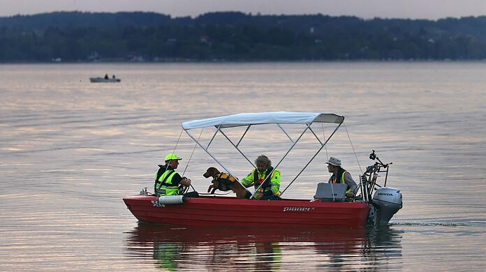 Ein Boot, mit einem Hundeführer und einem Hund, fährt in der Herrschinger Bucht auf dem Ammersee.
